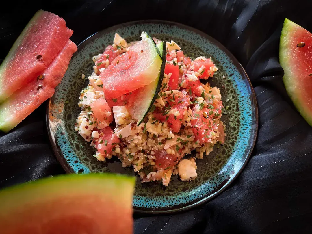 A small bowl holds this refreshing salad made with watermelon cut into large cubes, quinoa, feta, and turkey breast.