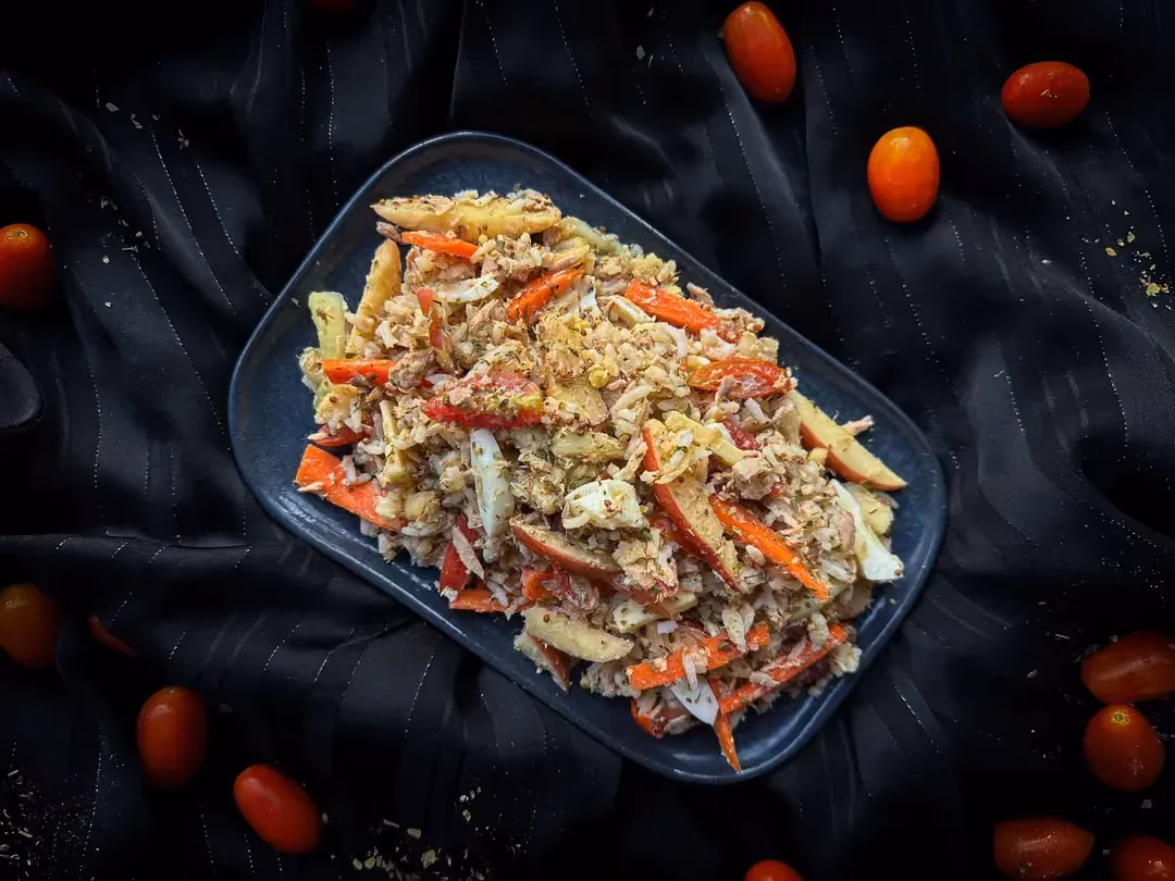 A shallow dish holds the rice salad with halved cherry tomatoes, tuna, and Comté. Tomatoes are placed next to the dish.