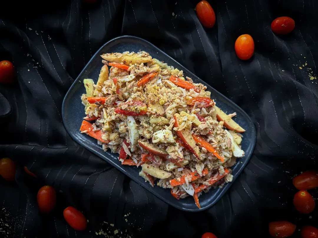 A shallow dish holds the rice salad with halved cherry tomatoes, tuna, and Comté. Tomatoes are placed next to the dish.