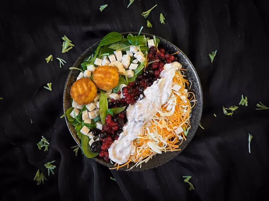 In a small salad bowl is a salad with red berries, breaded goat cheese, and diced chicken.
