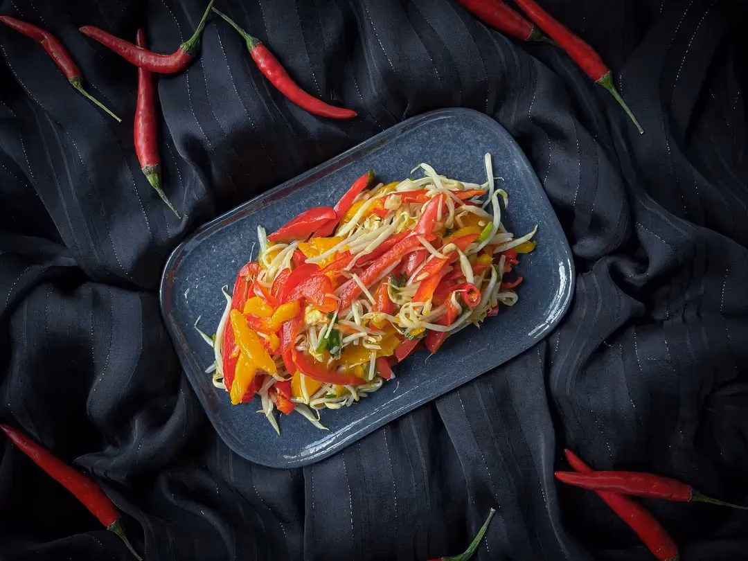 Un plat peu profond rectangulaire aux coins arrondis de couleur bleu accueille la recette de salade de mangues pimentée à la thaï.