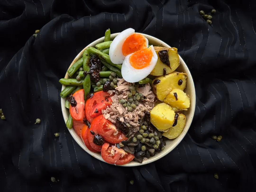 Dans un petit saladier en faïence blanc, se trouve mélangé pêle-mêle, les différents ingrédients de cette salade niçoise traditionnelle.