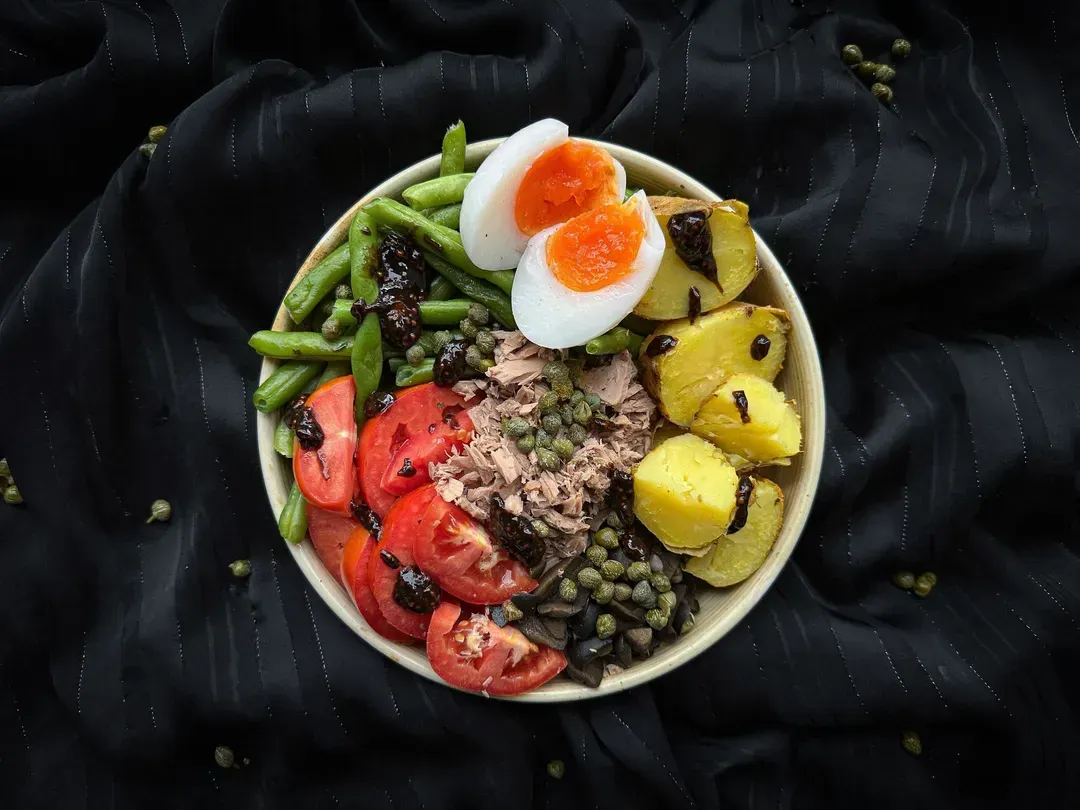 In a small white earthenware salad bowl, the different ingredients of this traditional Niçoise salad are mixed together haphazardly.