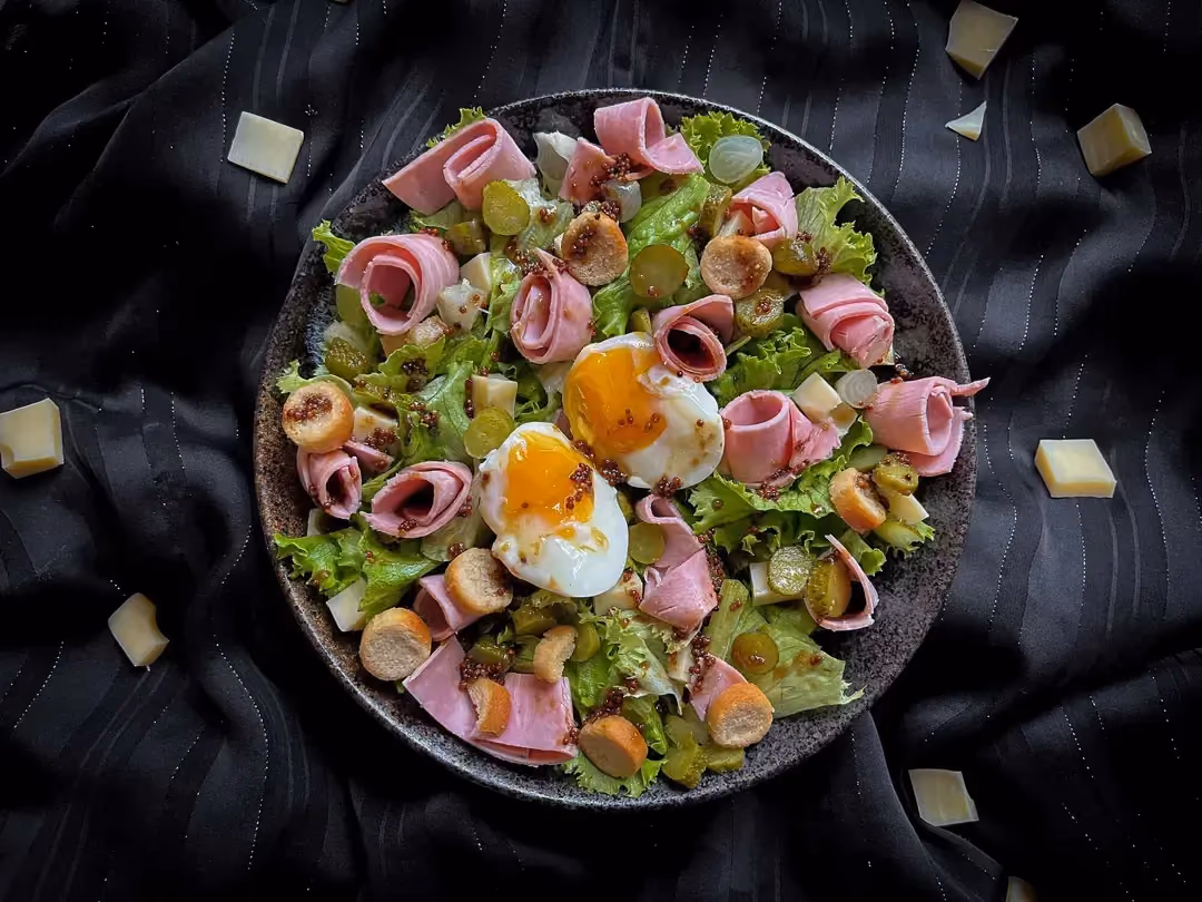 The Parisian salad, made with iceberg lettuce, emmental cut into small cubes, and ham cut into strips, is in a small salad bowl.