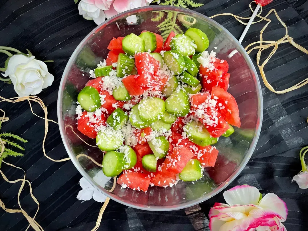 In a large transparent salad bowl, you can see the colors of summer with the red of the watermelon and the green of the cucumbers. Shredded coconut to finish.
