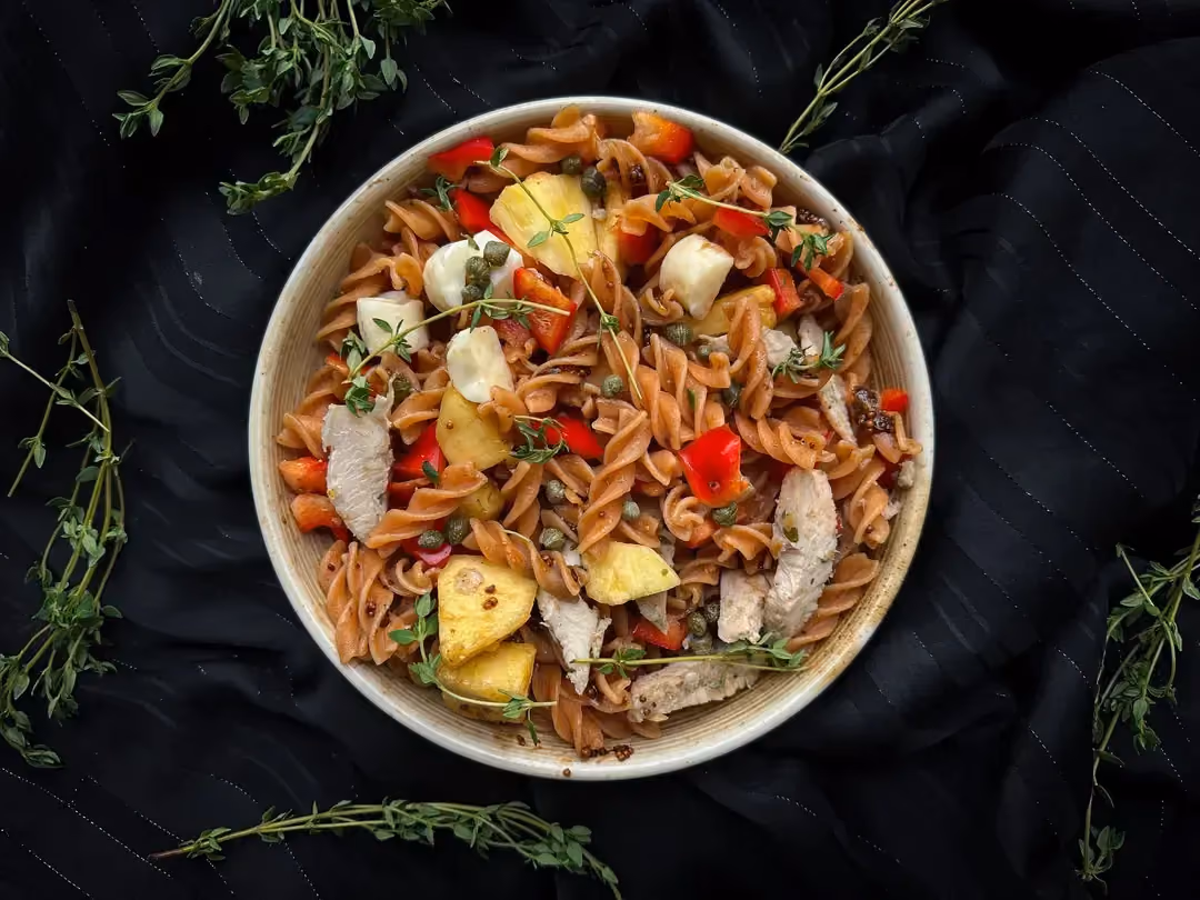 On a white plate, the pasta, chicken, pineapple, mozzarella, and bell pepper are mixed together.