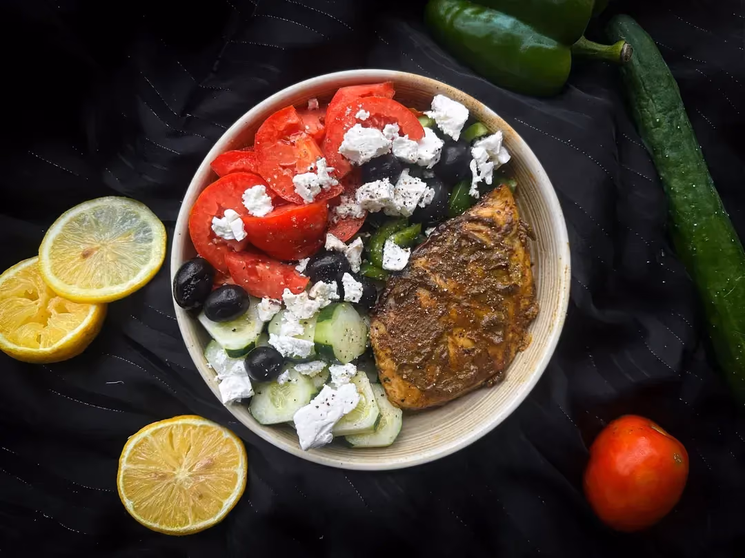 In a small white earthenware bowl is the Greek chicken salad recipe. A few black olives are there for decoration.