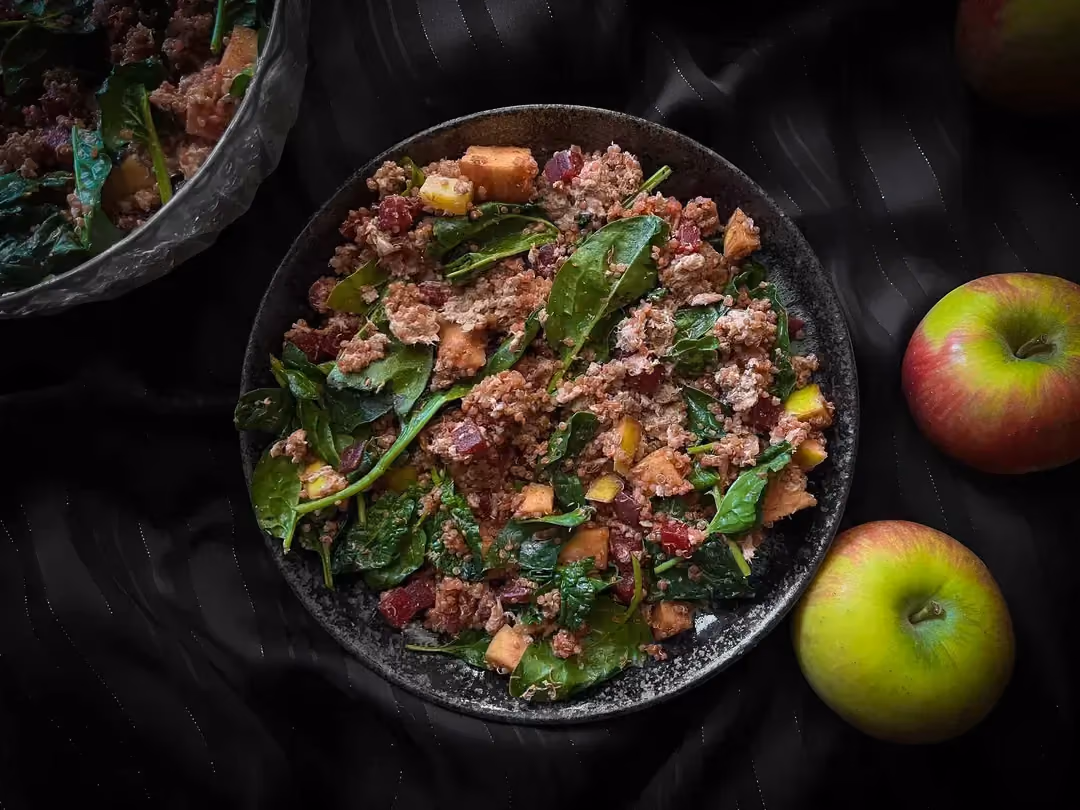 In a salad bowl, you'll find quinoa, beetroot, apples, spinach, Comté, and tuna. Two beautiful apples are next to the dish.
