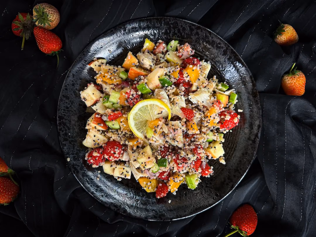 La salade de quinoa avec les fruits rouges, de la pomme et du poulet sont disposés sur une assiette plate de couleur noire.