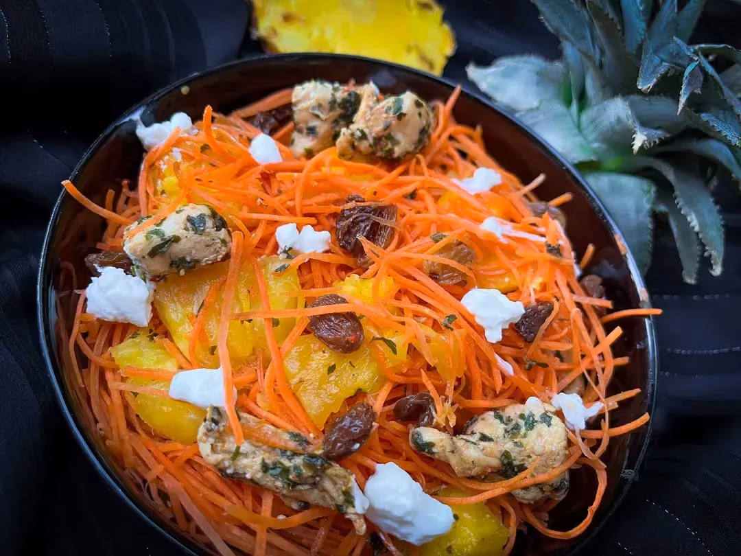 A small bowl holds the chicken salad with raisins, grated carrots, and pineapple cut into small cubes. Everything is mixed together.