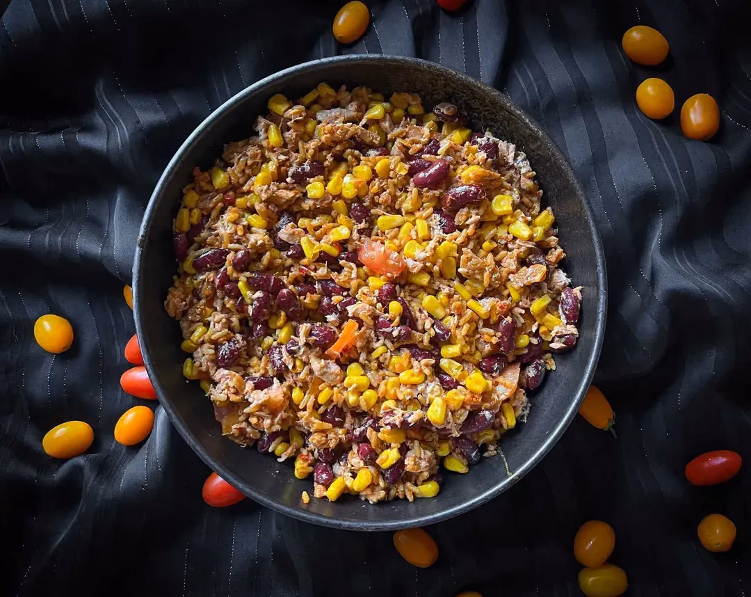 A blue bowl holds the rice salad with corn, kidney beans, tuna, and tomatoes.