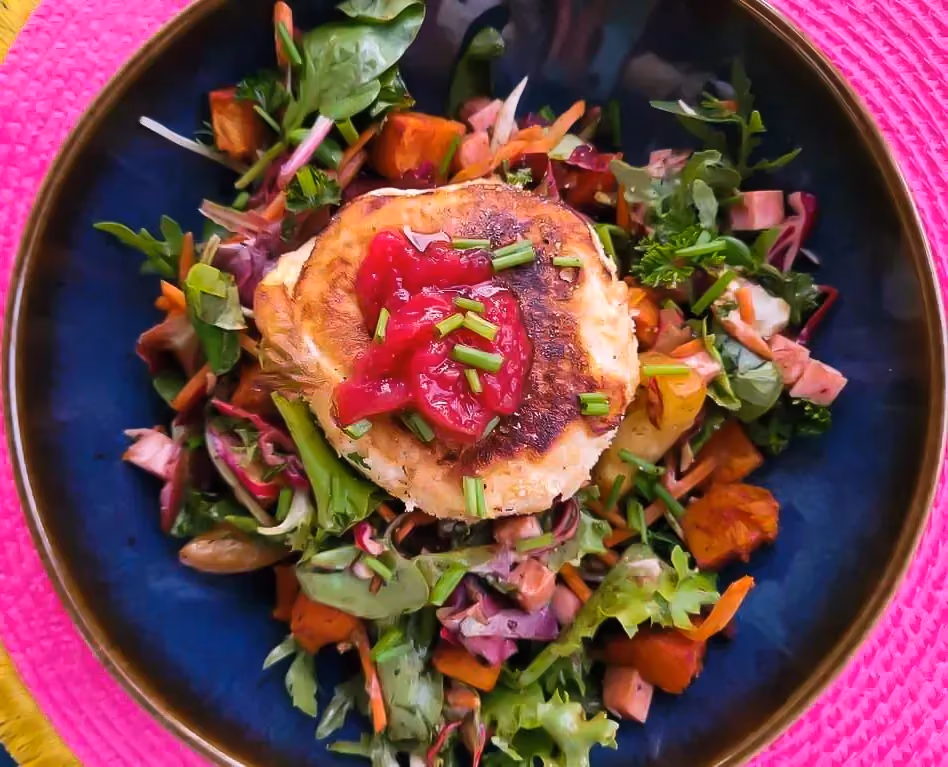 A salad with carrots, tomatoes, ham, and sweet potatoes, with roasted Tomme and strawberry jam in the center.