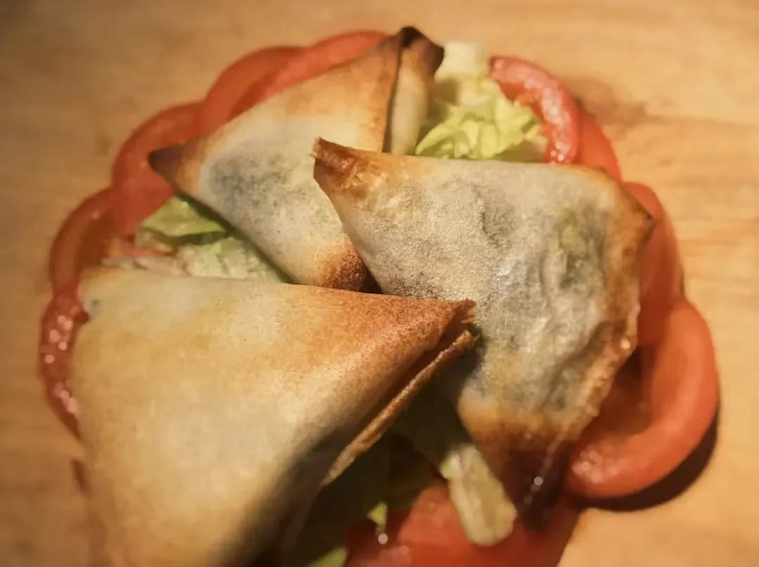Trois samoussas bien dorés sont disposés sur un lit de tomates coupées en fines tranches.