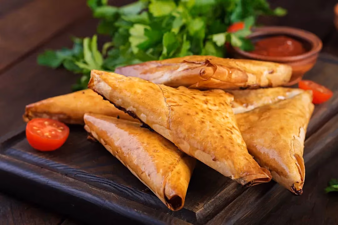 Au premier coup d'oeil on reconnait le samoussa avec sa forme triangulaire. Sur un plateau se trouve six samoussas avec une tomate coupée en deux.