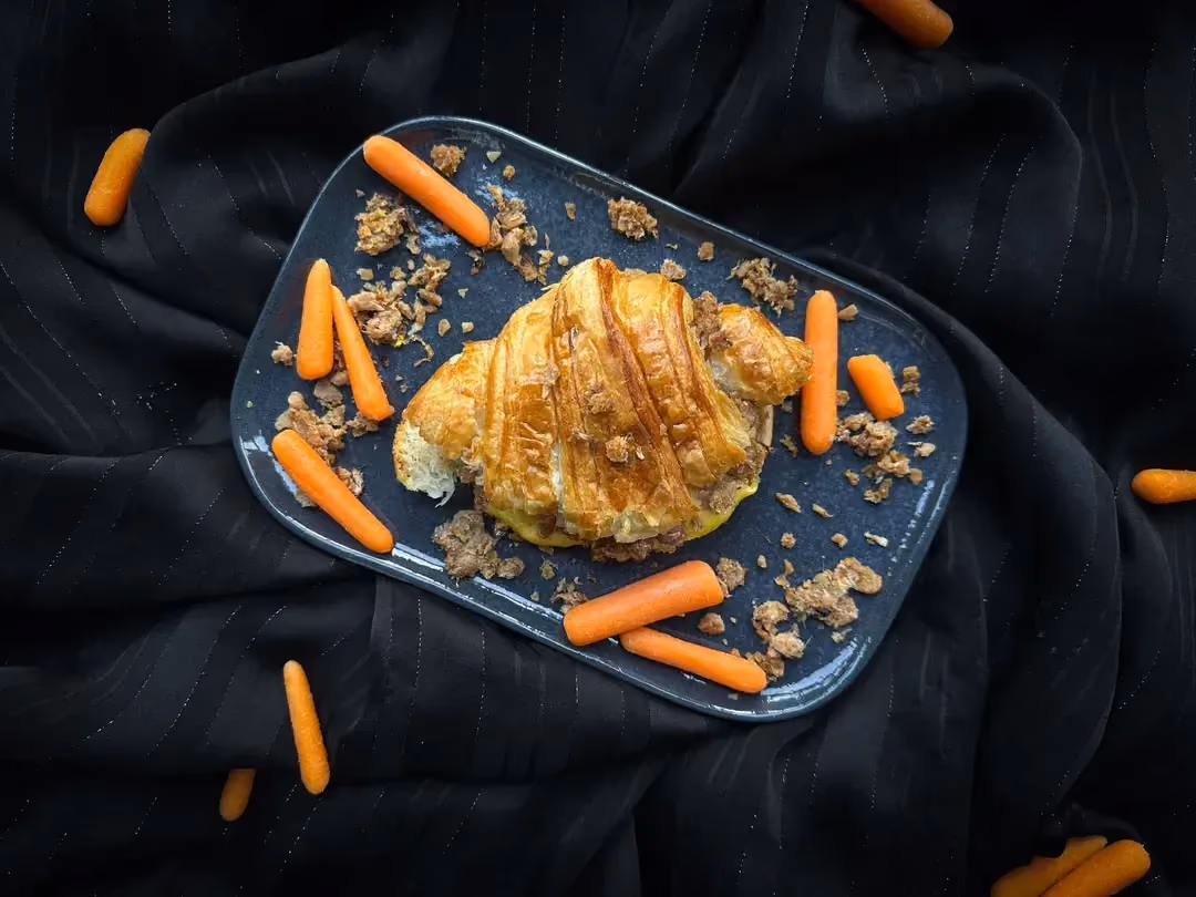 Un petit plat rectangulaire peu profond accueille le sandwich croissant au fromage et au boeuf. Des petites carottes sont présentent à côté du plat.