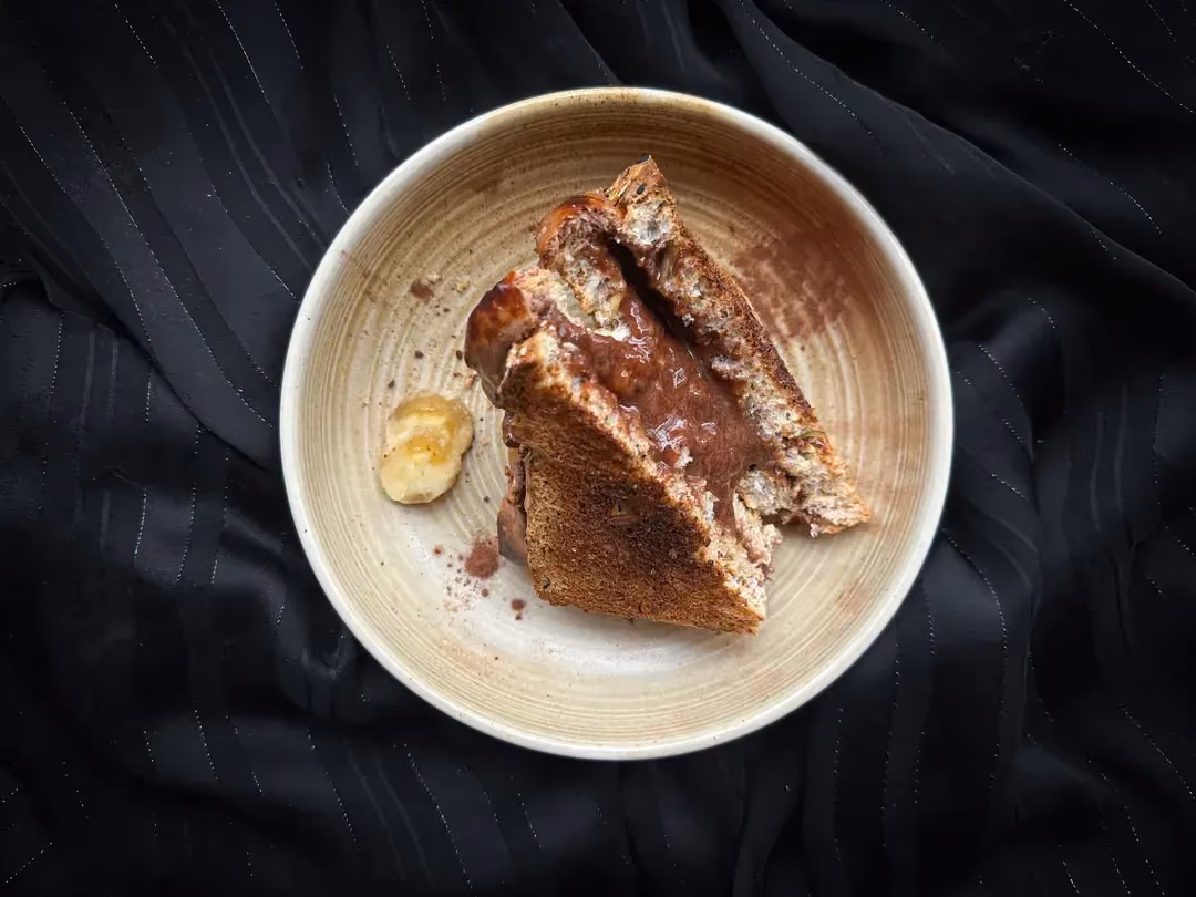 La recette de sandwich grillé à la banane et whey chocolat est présenté dans un petit bol en grès de couleur beige.