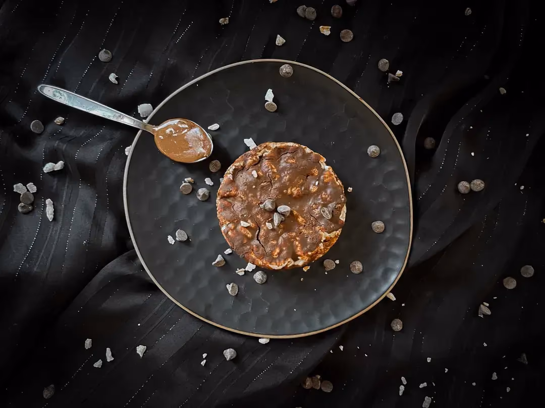 On a plate is the chocolate and peanut butter protein sandwich. A small spoon filled with chocolate is placed beside the plate.