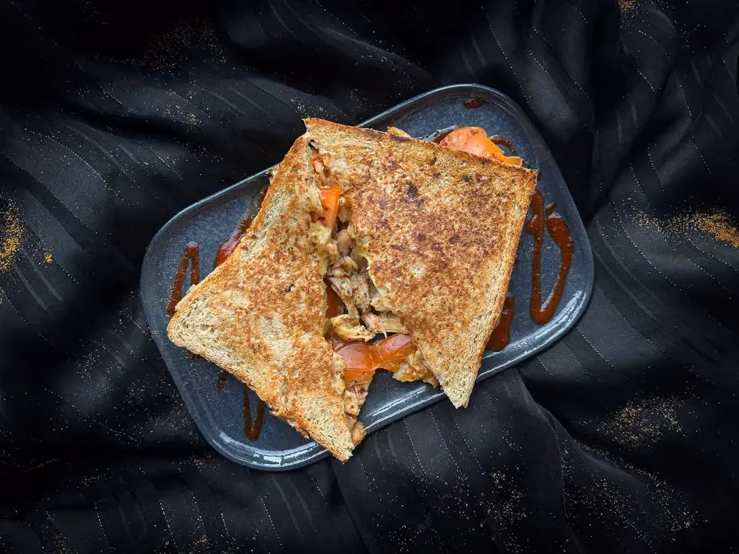 Two small chicken sandwiches with sriracha sauce and cheddar are placed on a blue rectangular plate.