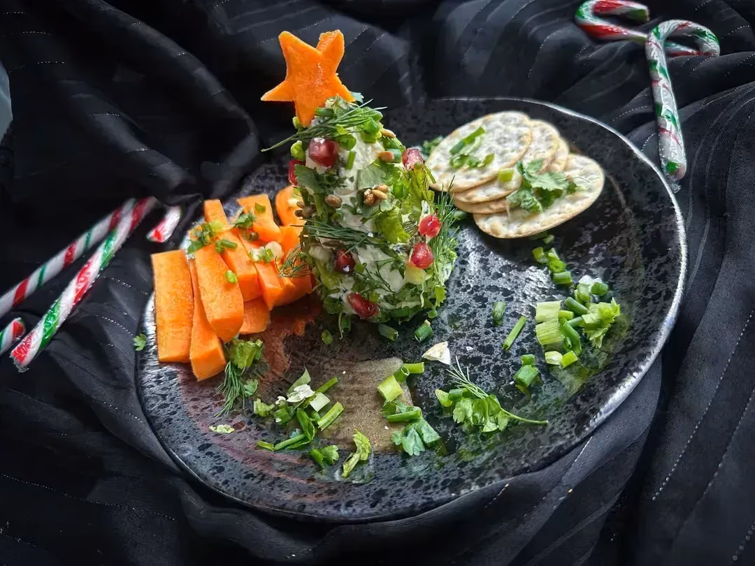The herb Christmas tree served with baby carrots and crackers is presented on a blue earthenware platter.