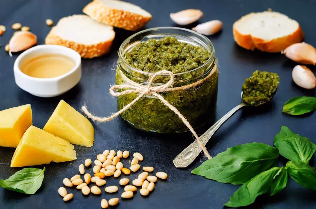 In a glass storage jar, "Le Parfait," is the pesto sauce. Next to it are Parmesan, garlic, and basil leaves.