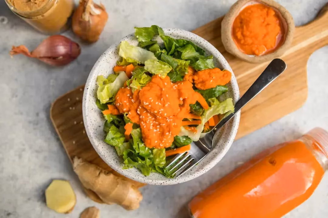Placed on a cutting board, a bowl contains salad served with carrot and ginger salad dressing.