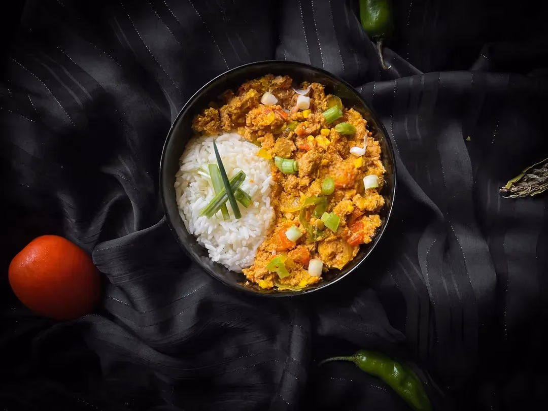 Un petit saladier contient d'un côté du thon émietté avec des petits morceaux de gros piment et de l'autre du riz blanc.