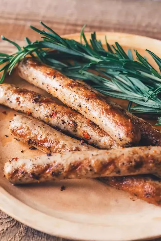 Sur une assiette en grès, à coté d'une branche végétale qui donne un côté champêtre à ce plat, se trouve quatre saucisses veggie bien grillées.
