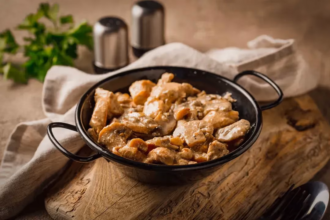 The forest-style seitan is presented in a black wok on a brown countertop.