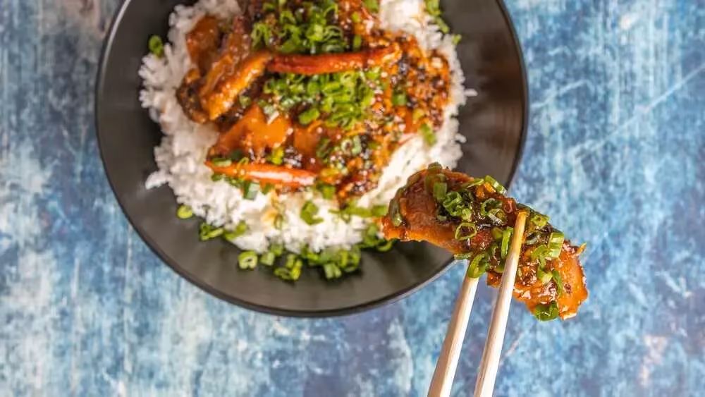Sur un lit de riz blanc, se trouve de gros morceaux de seitan colorés par les oranges et parsemés d'oignons verts finement ciselés.