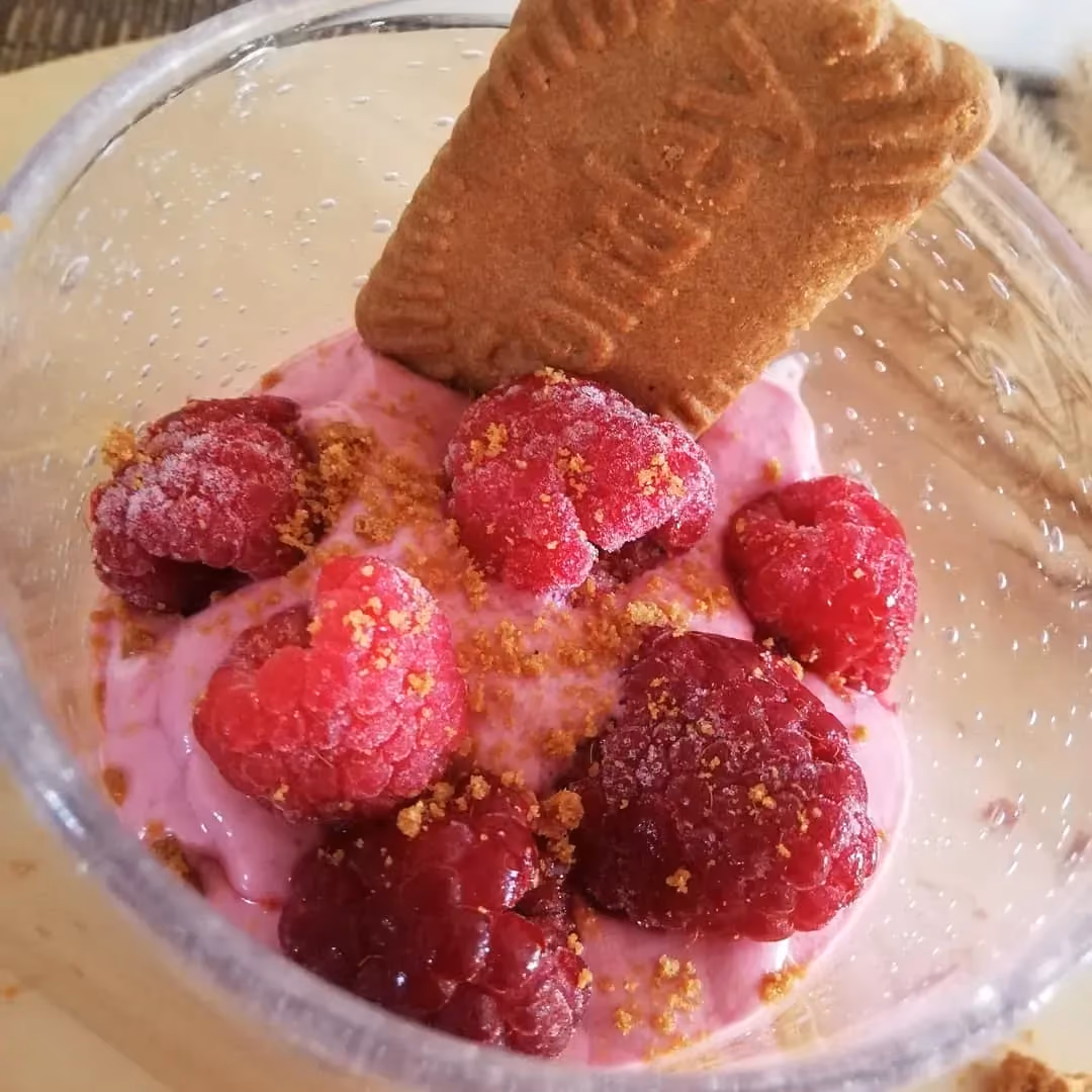 Dans un grand verre se trouve un smoothie, avec sur au dessus de grosses framboises et un spéculoos.