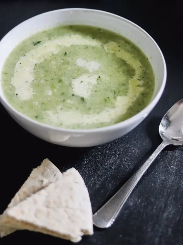 Dans un bol en faïence blanc se trouve la soupe de courgettes et Vache qui rit. Deux portions de fromage sont posée l'une sur l'autre.