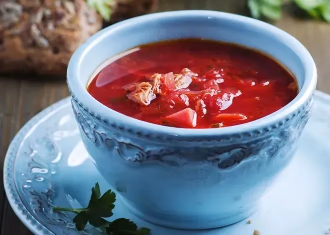 In a blue earthenware bowl is beet soup with its beautiful purple color. A small bunch of parsley is placed next to it.