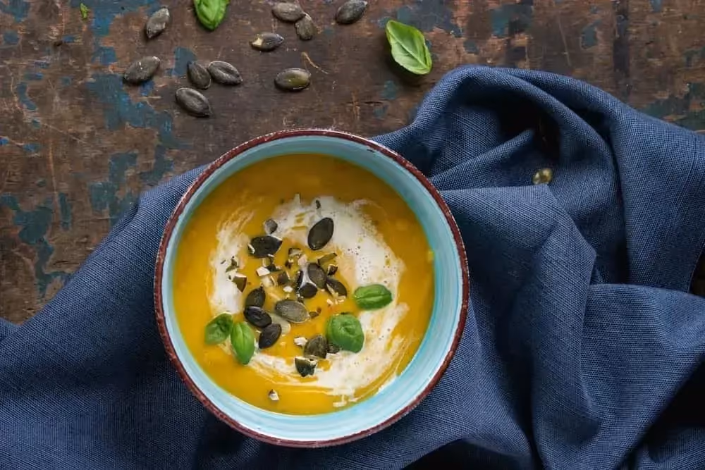 Posé sur une serviette de couleur bleue, se trouve un large bol contenant la soupe de patate douce, poireaux et coco.