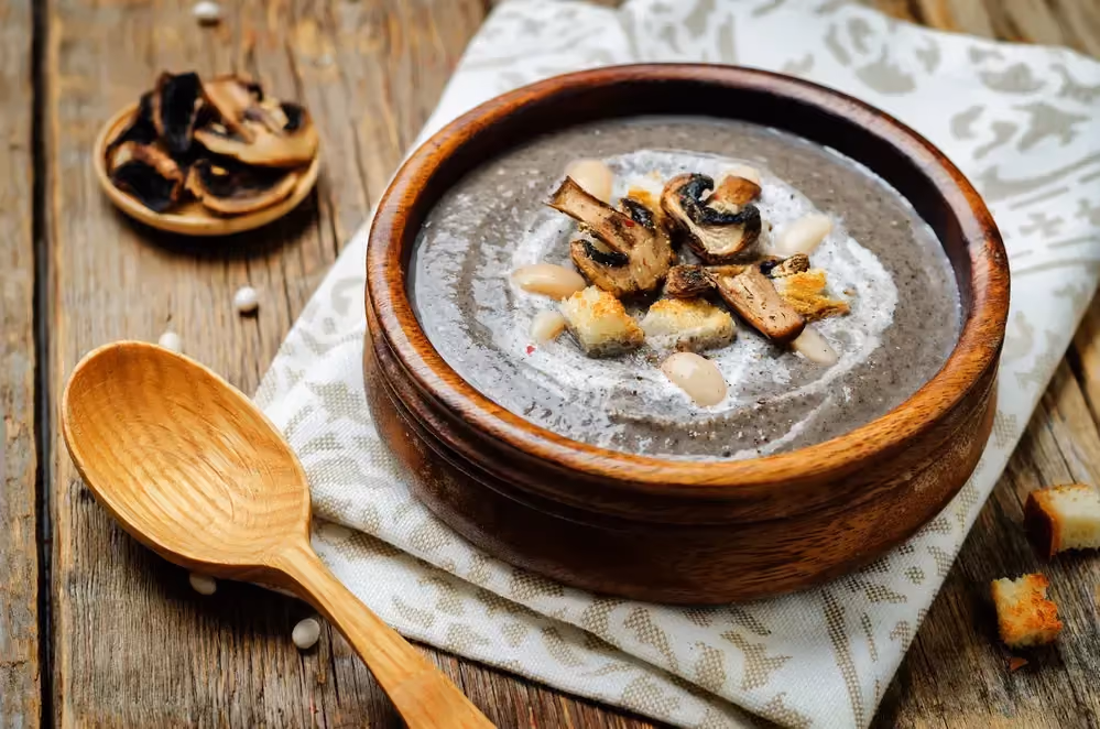 On a rustic wooden table, there is a dish towel with a terracotta soup tureen placed on it, containing the red bean soup.