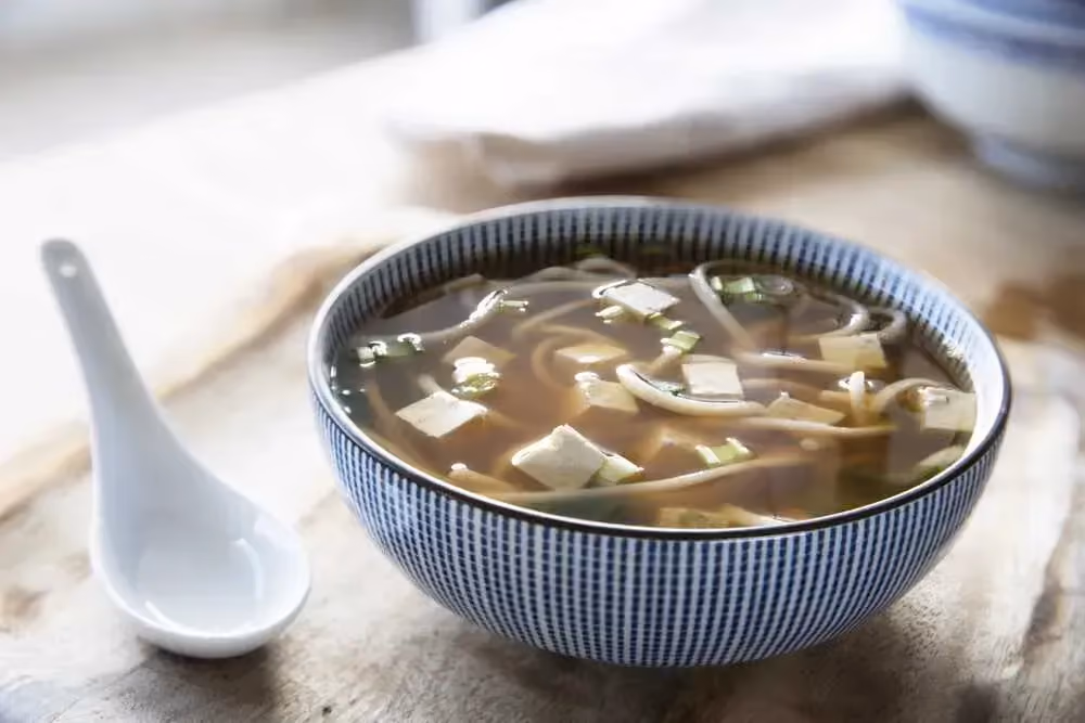 Miso soup is presented in a blue-and-white earthenware bowl. A traditional spoon is placed next to the bowl.