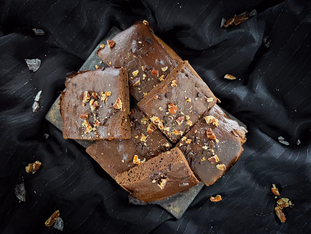 Le brownie protéiné est présenté sous la forme d'une pyramide du plus bel effet ! Des noix sont visibles près du dessert.