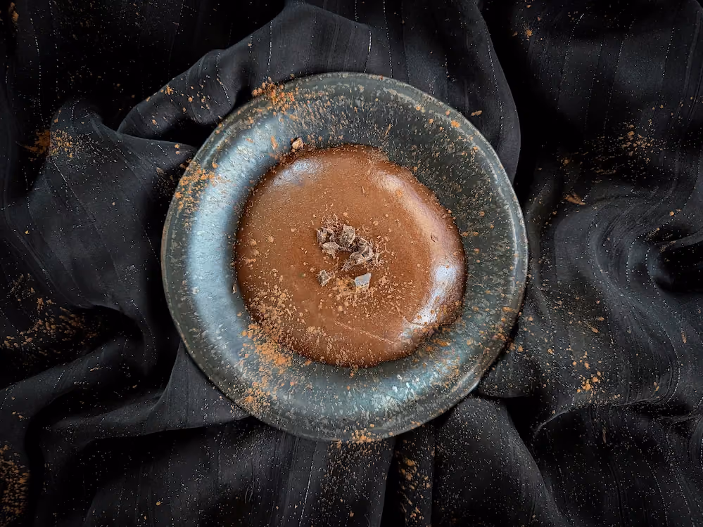 Dans un plat creux en faïence bleu se trouve un flan au chocolat du plus bel effet. Le topping est assuré par un morceau de chocolat aux noisettes.