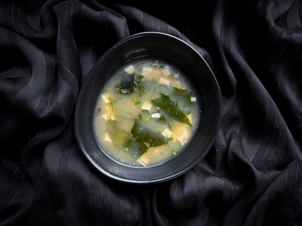 La soupe miso est présentée dans un bol en faïence bleu et blanc. Une cuillère traditionnelle se trouve à côté du bol.