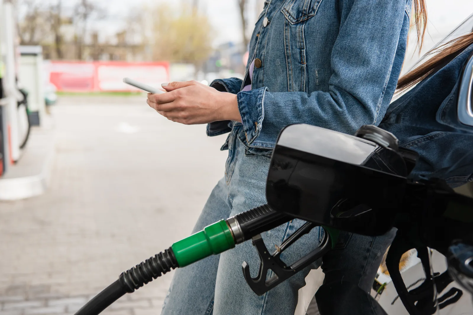 Woman using smartphone while refueling car at gas station