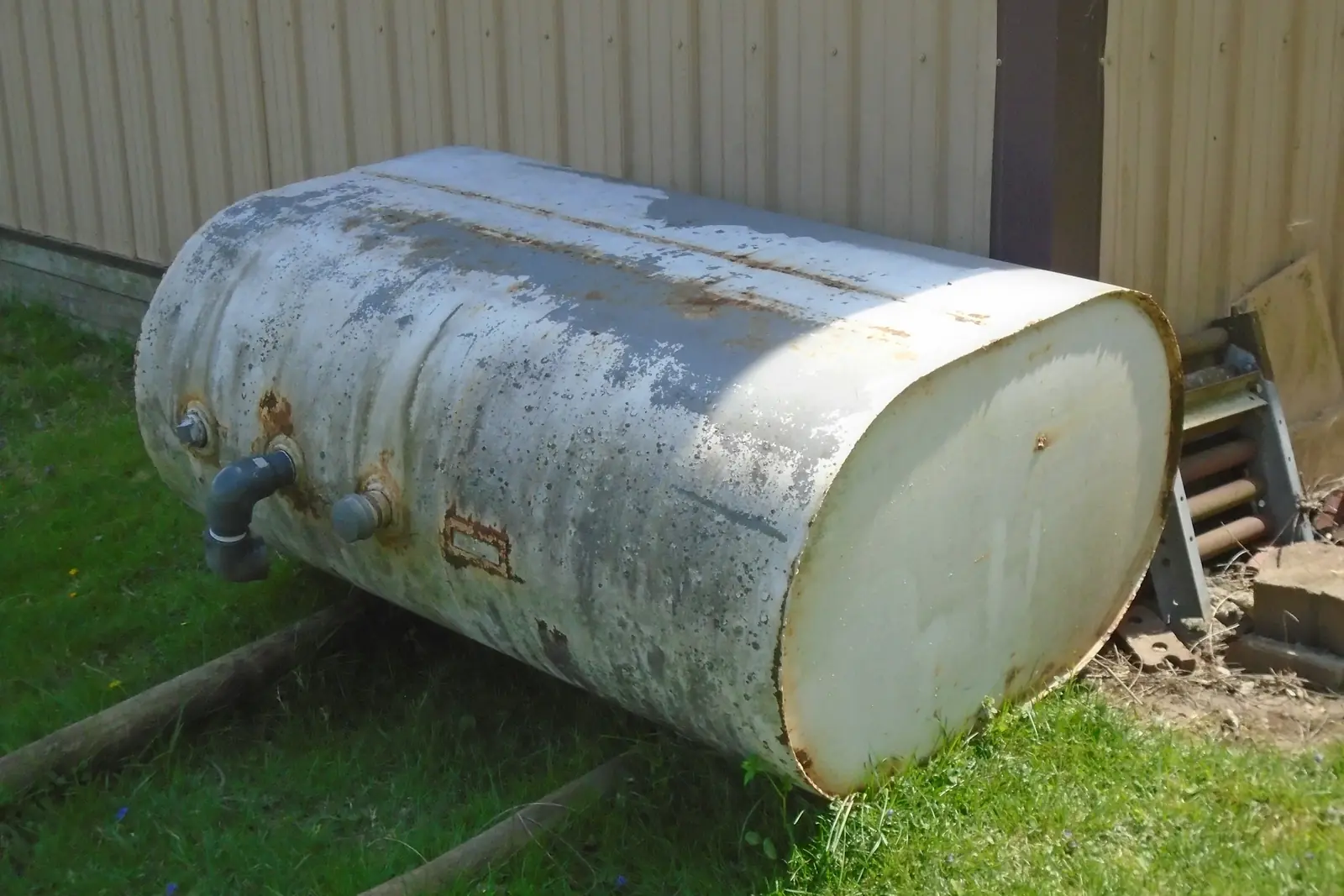 A weathered aboveground steel storage tank resting on timber skids beside a metal-clad commercial building, showing the wear an owned tank picks up over its working life