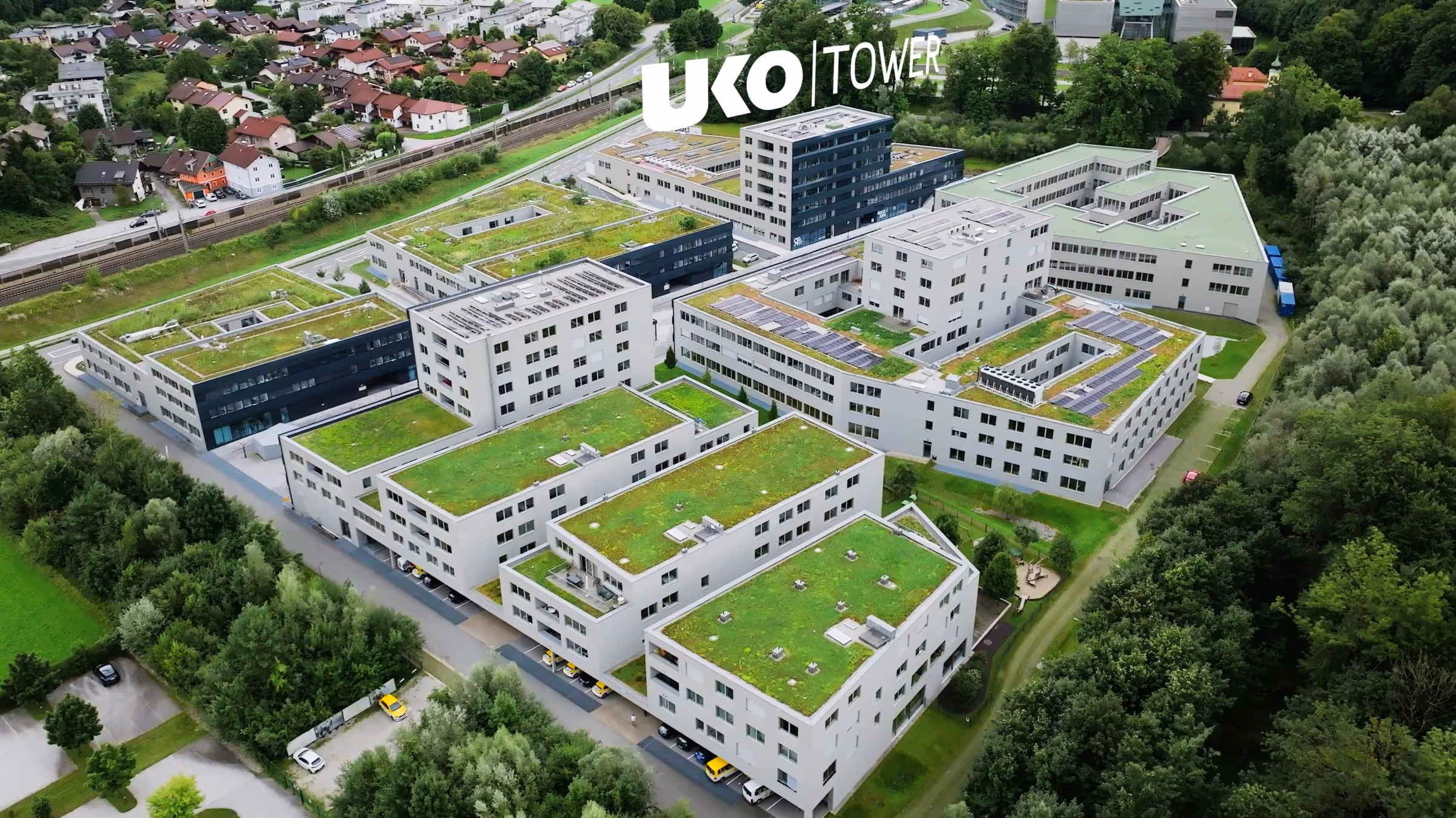 Luftaufnahme eines modernen Bürogebäudekomplexes mit begrünten Dächern und Solarpanelen, umgeben von Bäumen und Wohnhäusern.