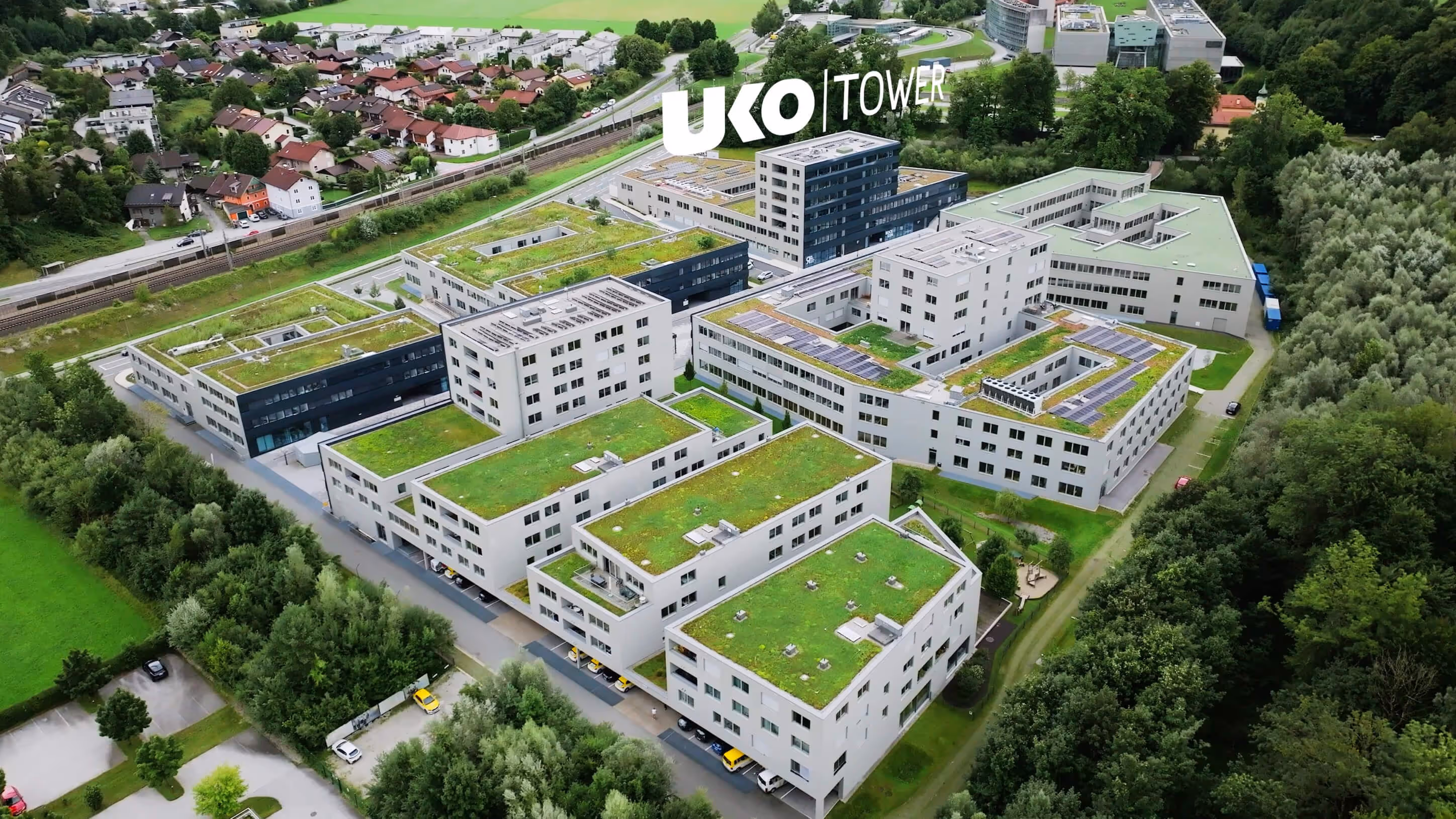 Luftaufnahme moderner Bürogebäude mit begrünten Dächern, umgeben von Bäumen und einer Wohnsiedlung im Hintergrund.