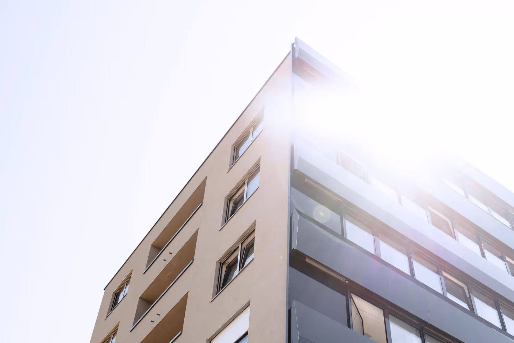 Blick von unten auf eine moderne, mehrstöckige Wohnung mit Balkonen und Sonnenlicht von rechts oben.