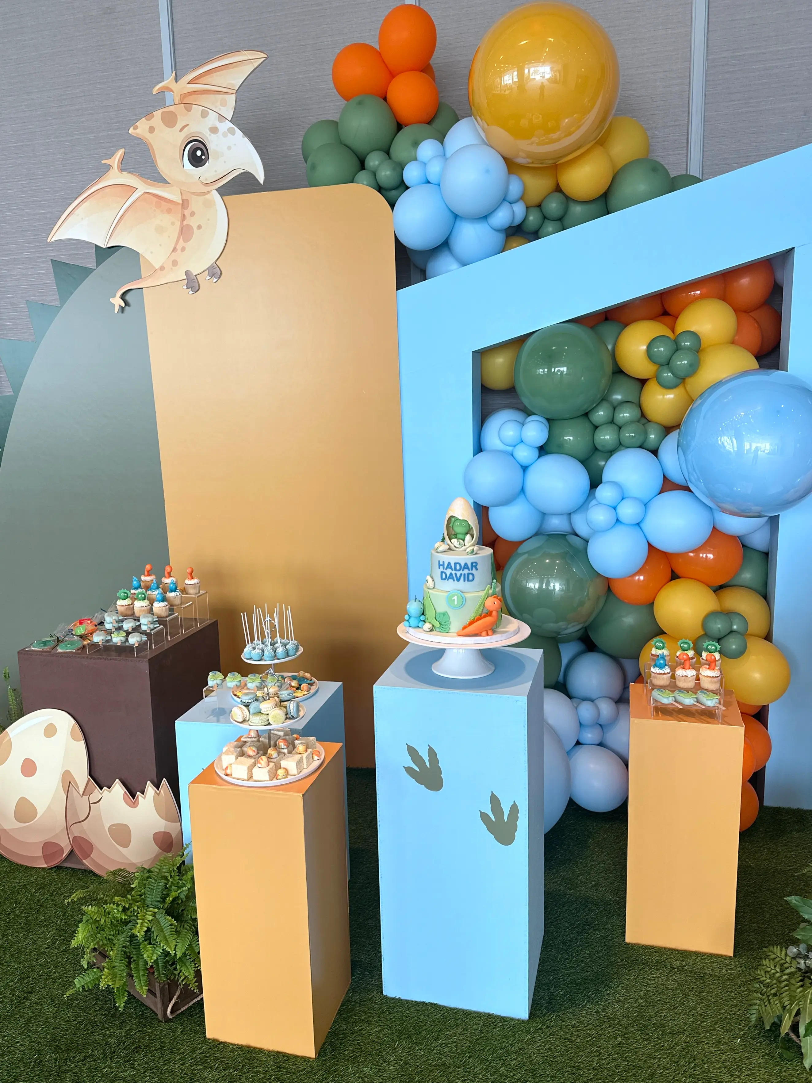 Dinosaur-themed birthday cake and dessert table at parklane hotel in limassol cyprus, featuring custom baby dinosaur cake, colourful balloon installation, and coordinated sweets display for a first birthday celebration