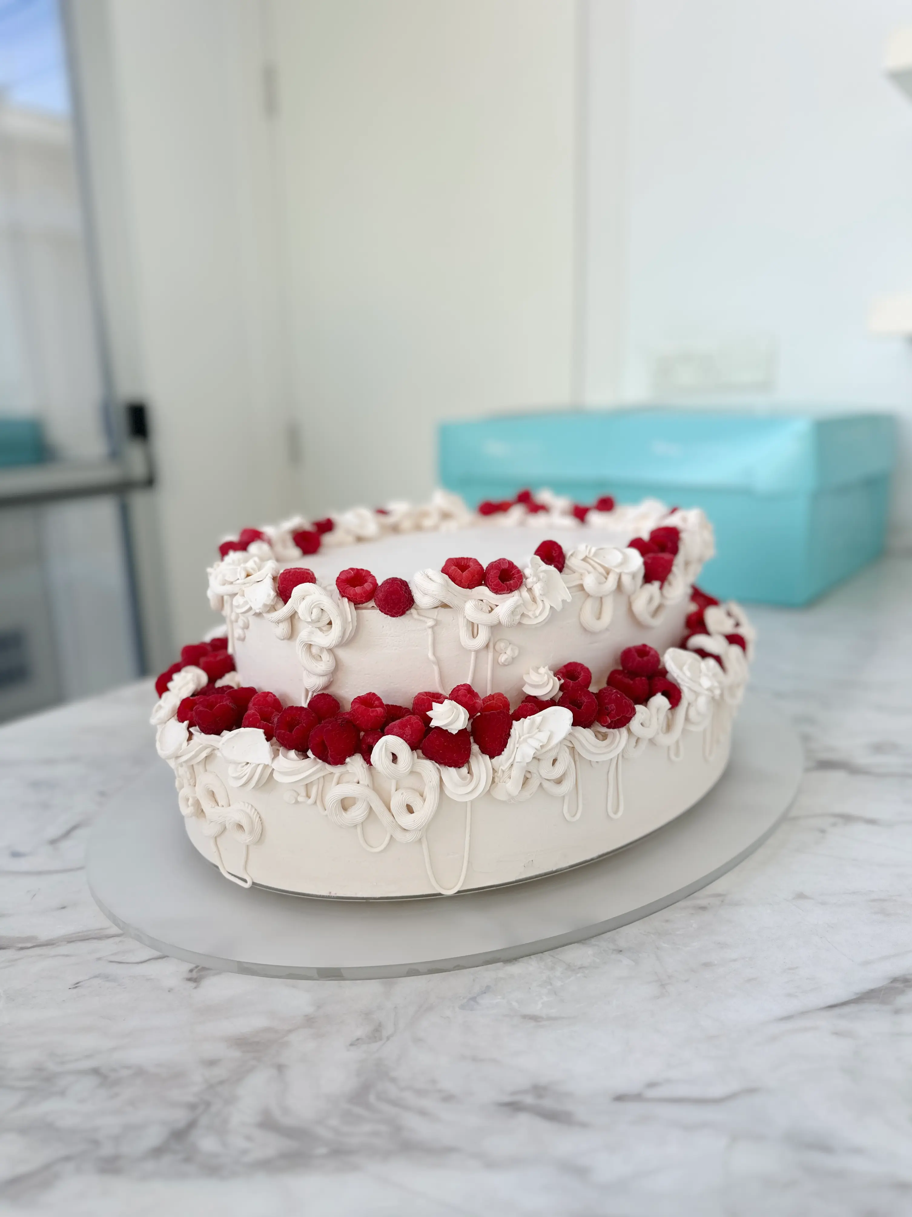 Modern two-tier wedding cake with textured white frosting, delicate piped details and fresh raspberries, minimalist romantic style in Limassol Cyprus