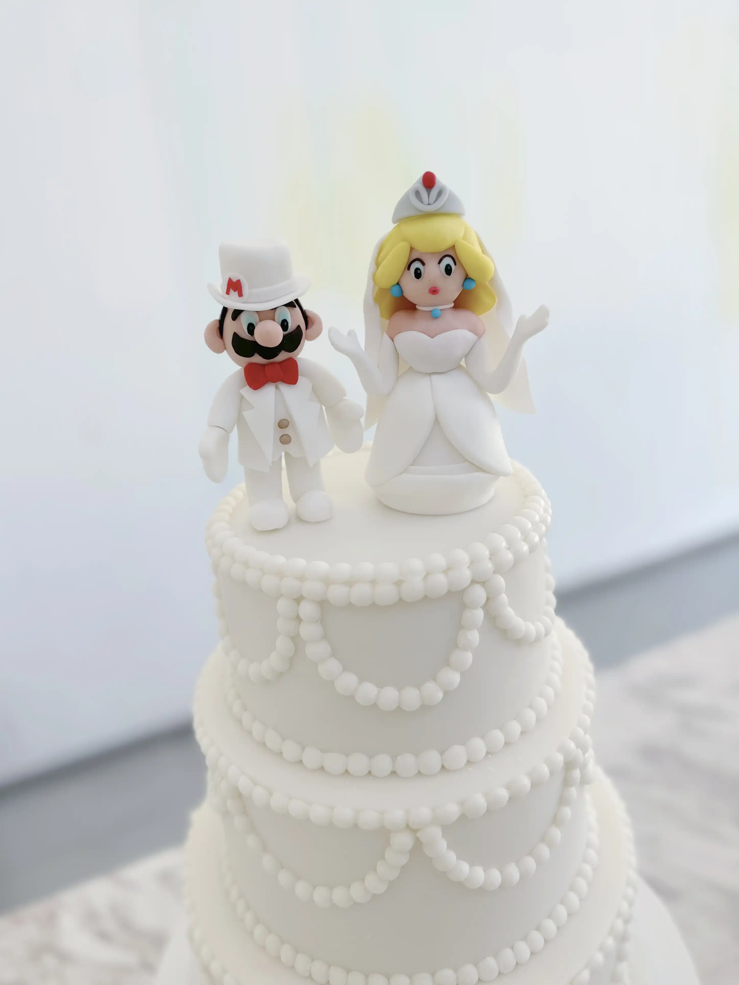 Elegant three-tier white wedding cake with pearl garland piping and custom super mario groom and bride figurines, classic luxury design