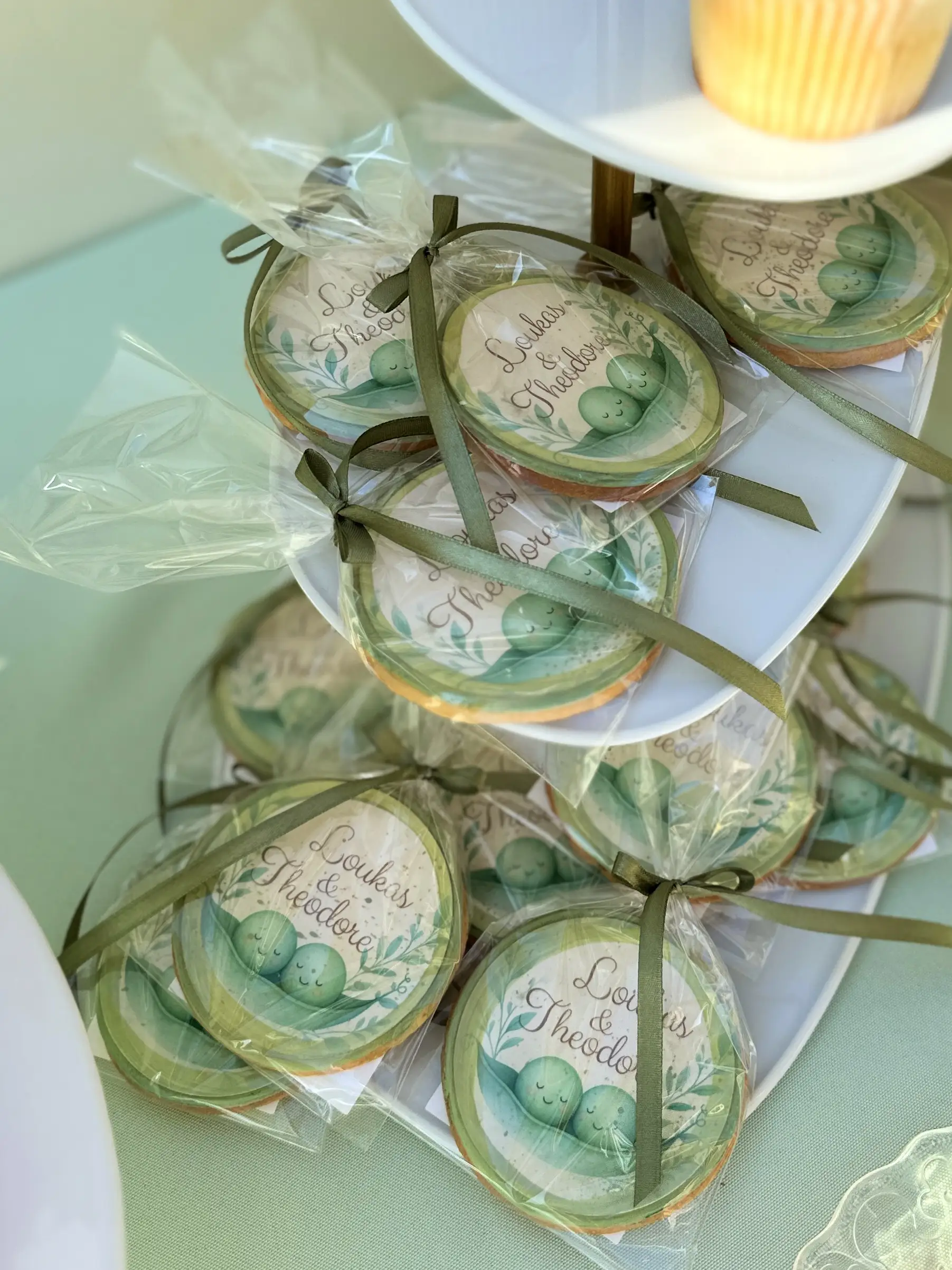 Custom decorated cookies as christening favours for twin boys, “two peas in a pod” theme with personalised names, individually wrapped with elegant green ribbon, coordinated dessert table details