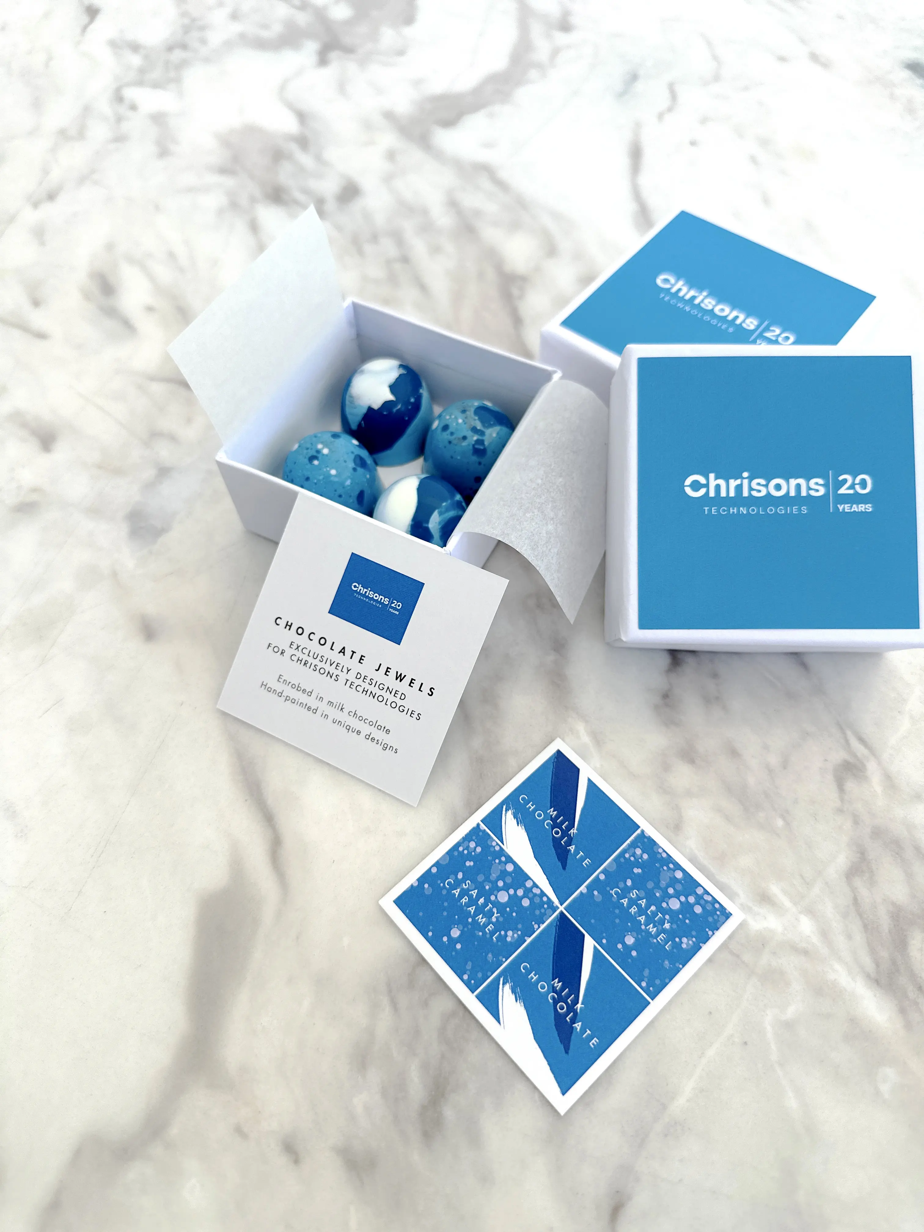 Luxury corporate chocolate bonbon gift box with blue branded packaging, featuring hand-painted chocolates in white and blue tones, presented with custom printed card for company anniversary celebration