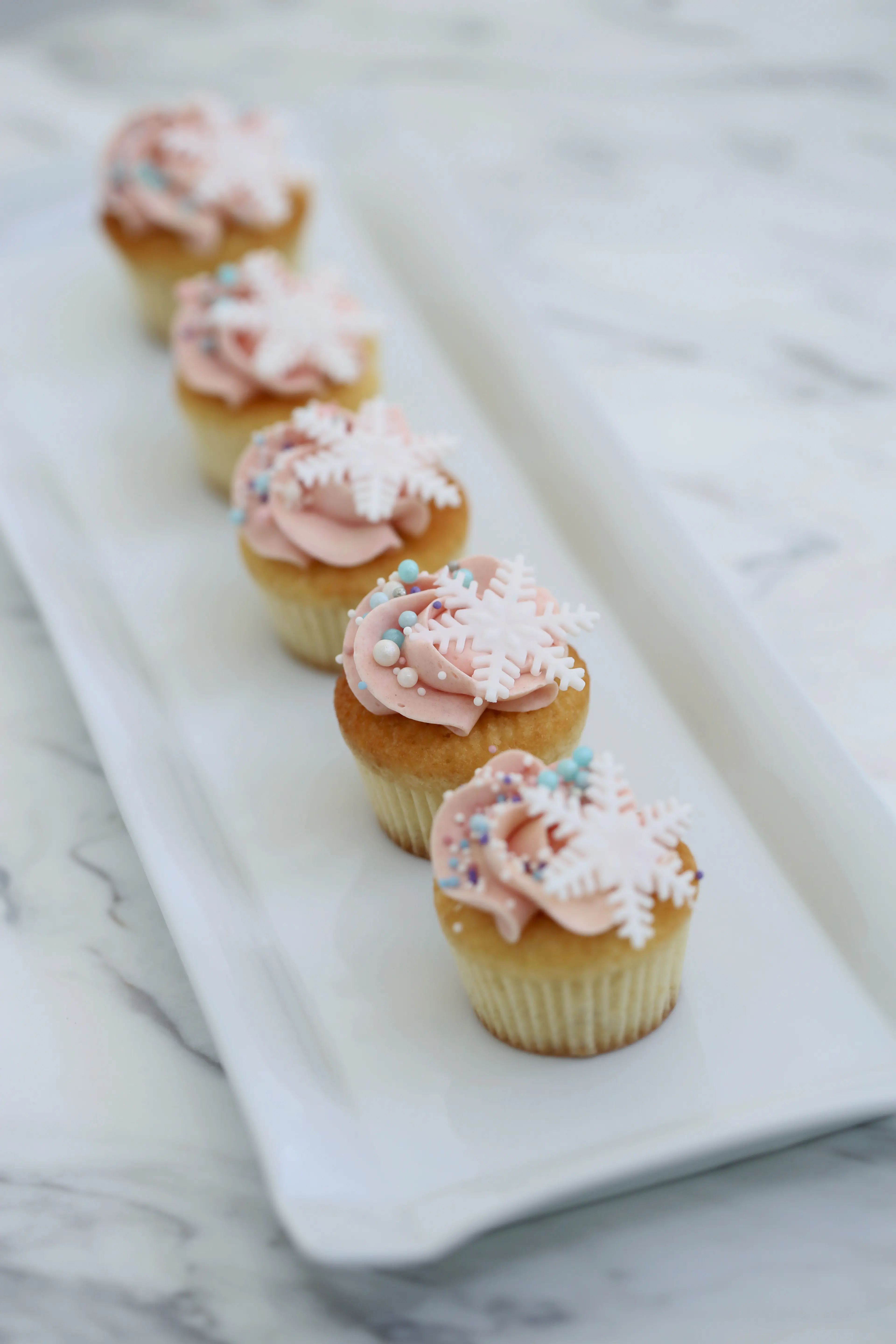 Mini vanilla cupcakes with soft pink buttercream, snowflake toppers and delicate sprinkles, elegant bite-sized desserts for events in limassol cyprus