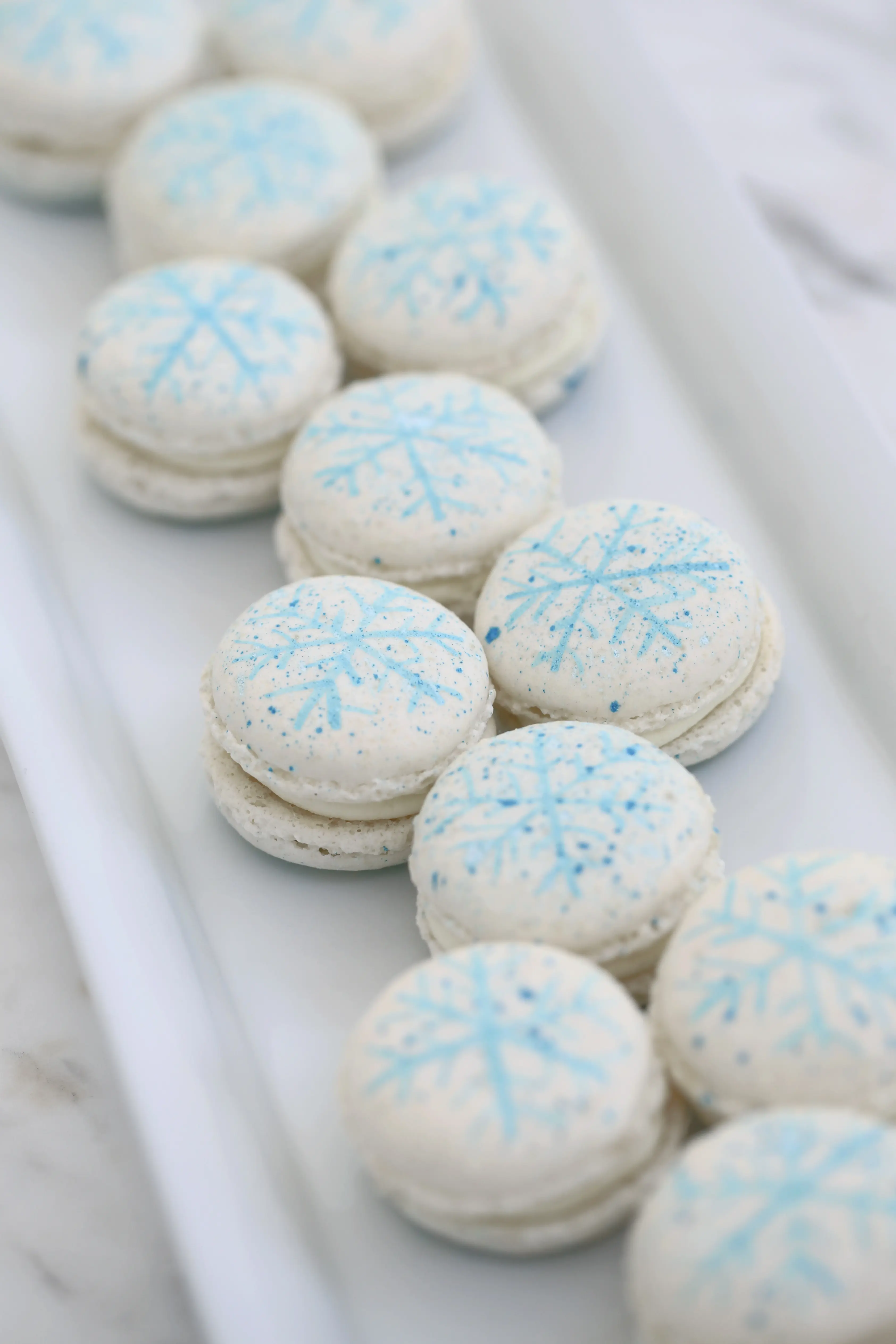 White macarons with hand-painted blue snowflake design, refined french pastries perfect for winter dessert tables in limassol cyprus